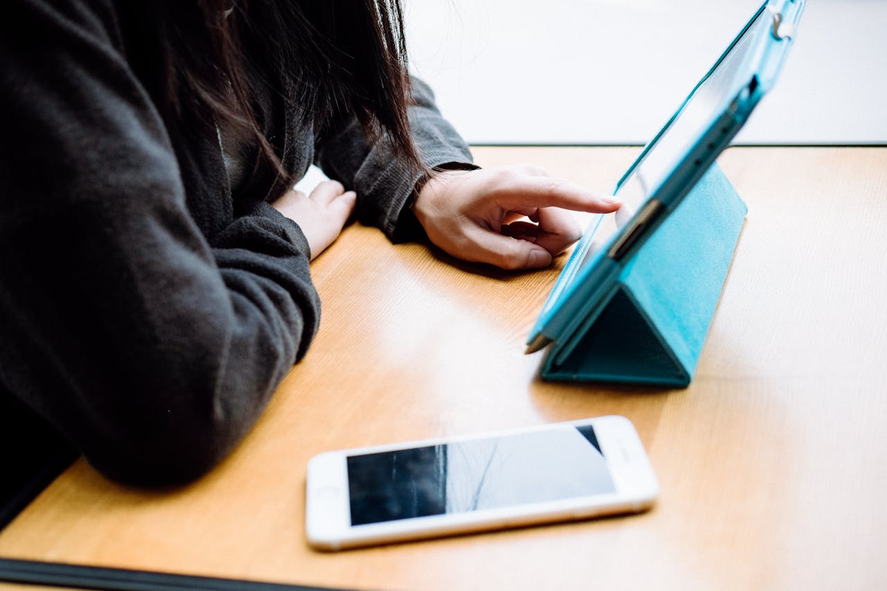 A person interacts with a tablet on a table, next to a smartphone, showcasing modern digital habits.