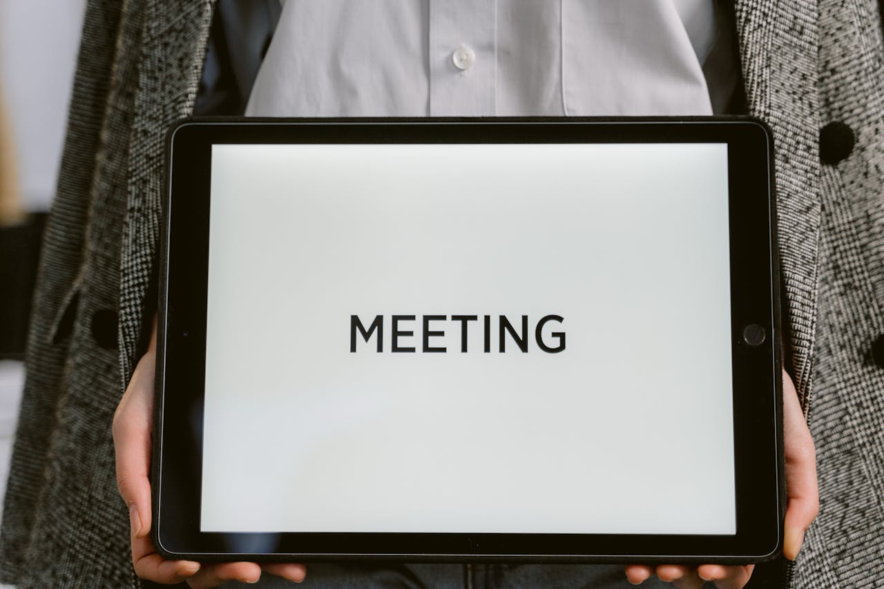 Close-up of a tablet with 'MEETING' on the screen held by a person in a blazer.